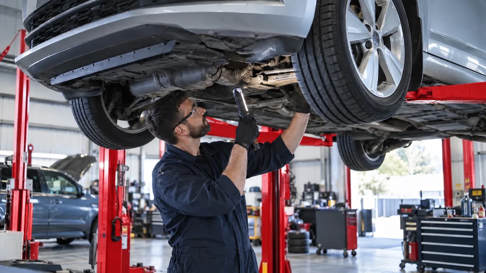 Technician inspecting the underside of a vehicle on a workshop lift
